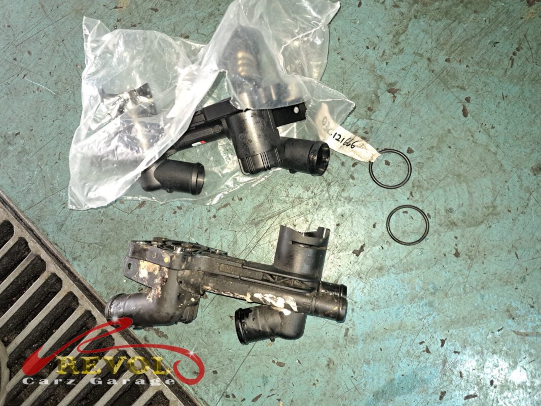 The old thermostat housing module (bottom, coolant-crusted) beside the new VAG-spec unit (top) with fresh O-rings.