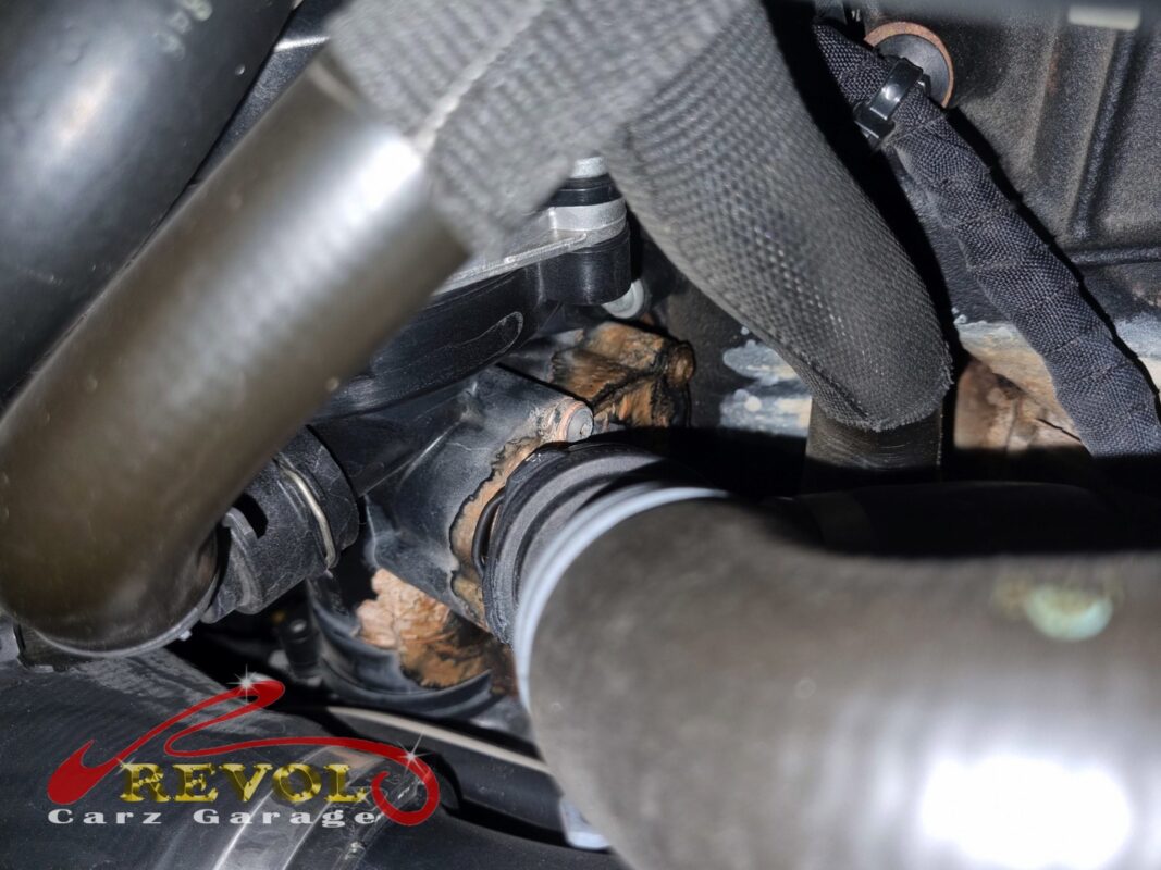 The thermostat housing area at the back of the engine, the cracked plastic and dried coolant visible.