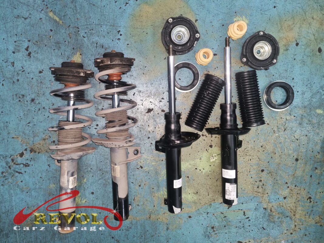 The two old front strut assemblies (left) beside the new VAG-spec pair (right), with new top mounts, bump stops and boots.