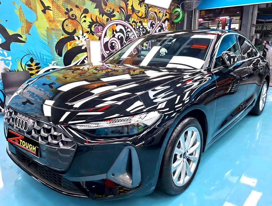 Black Audi A5, front three-quarter view, in the Revol Carz Makeover workshop with ceiling lights reflected on the bonnet.