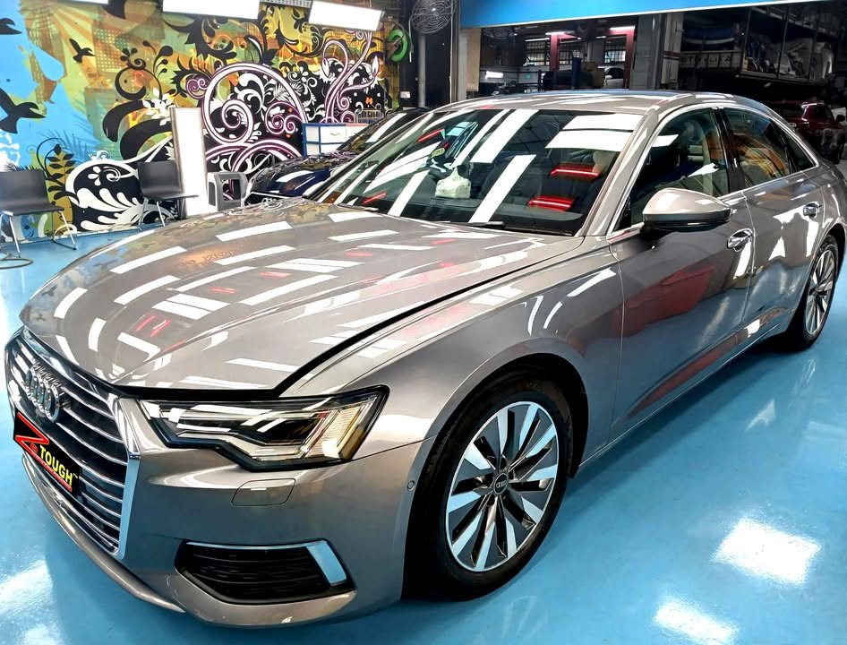 Grey Audi A6 sedan, front three-quarter view, with ceiling lights reflected on the bonnet after its ZeTough Ceramic coating.