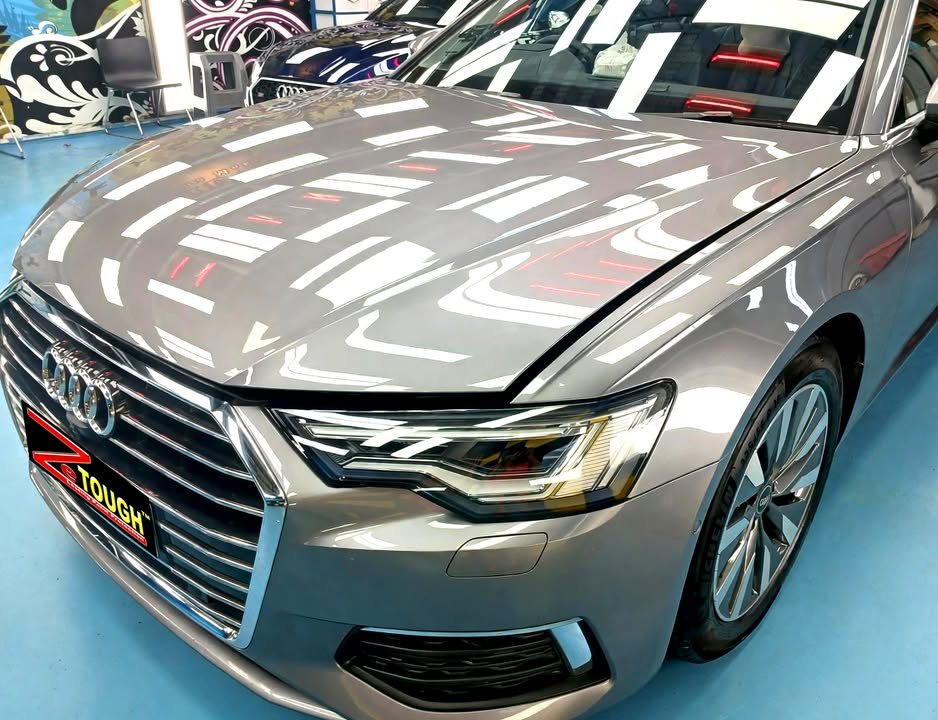 Close-up of the Audi A6 grille, headlamp and bonnet reflecting the workshop lights.