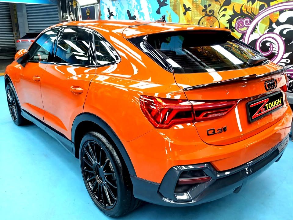 Rear three-quarter view of the orange Audi Q3 showing the tail lights and black alloy wheel.