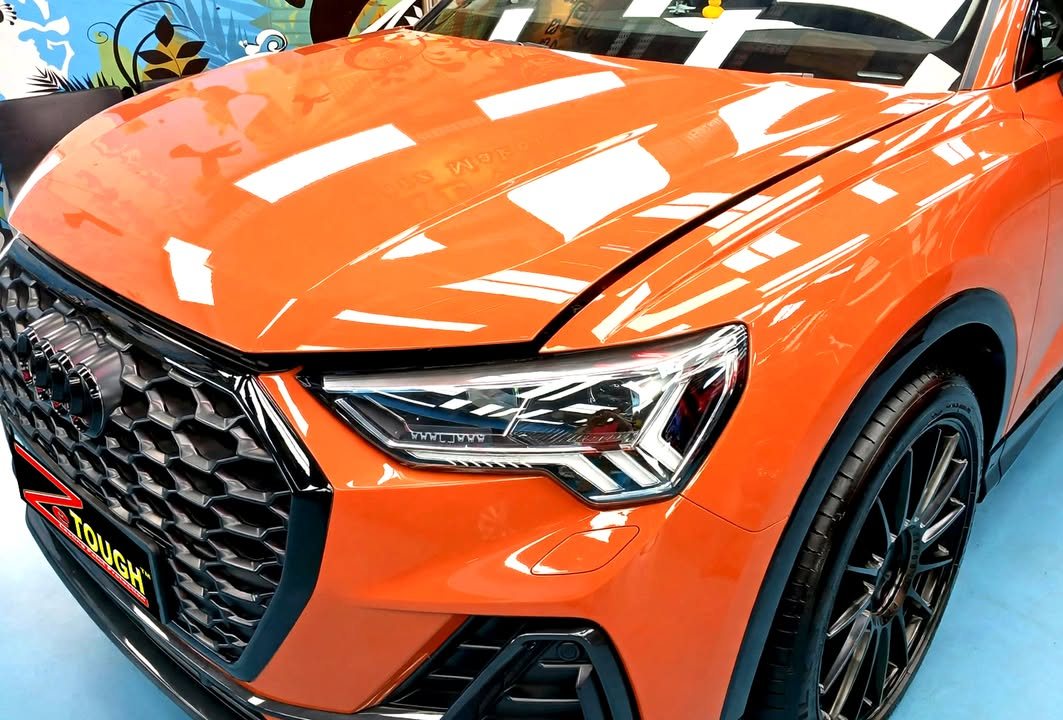 Orange bonnet and black grille of the Audi Q3 reflecting the ceiling lights.