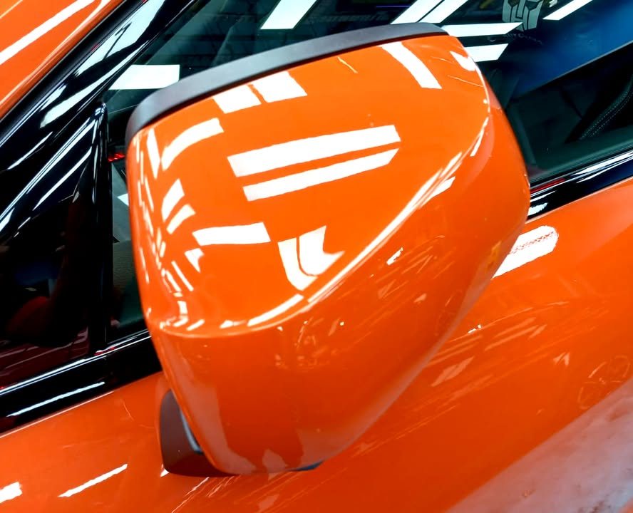 Orange side mirror cap with reflections of the ceiling lights.