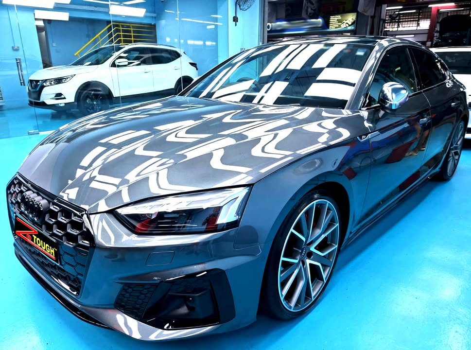 Front three-quarter view of a grey Audi S5 Sportback in the Revol Carz Makeover studio, ZeTough plate on the front bumper.