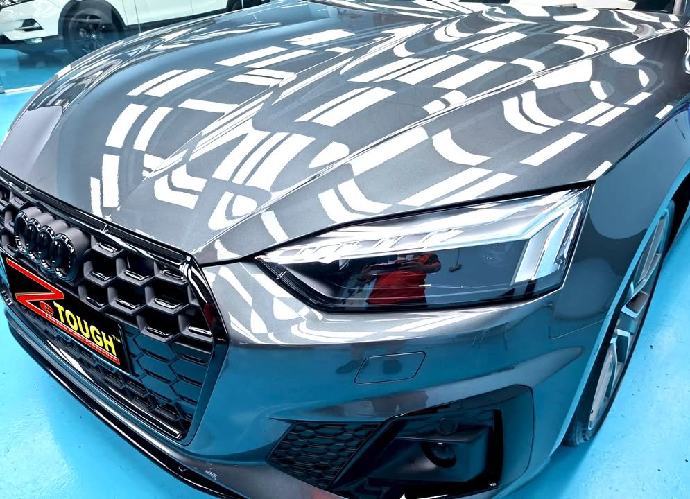 Close-up of the Audi S5 grille and headlight with studio lights reflected in the grey bonnet.