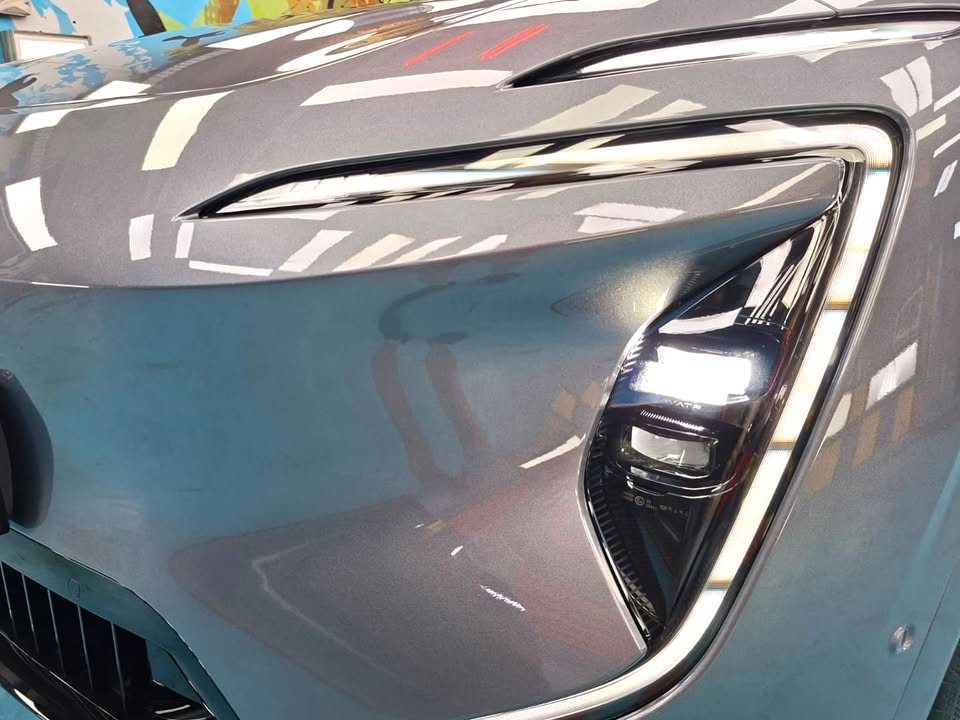 Close-up of the headlight and front panel with sharp light reflections in the grey paint.