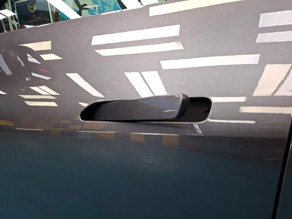 Flush door handle on the grey door panel, with ceiling lights reflected across the paint.