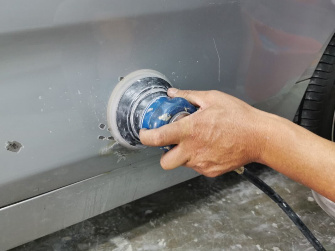 Machine-sanding a panel on the BMW 2 Series back to a smooth surface.