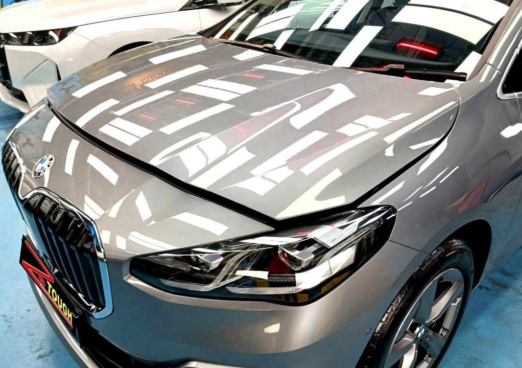 Front of the grey 2 Series with ceiling lights reflected across the bonnet.