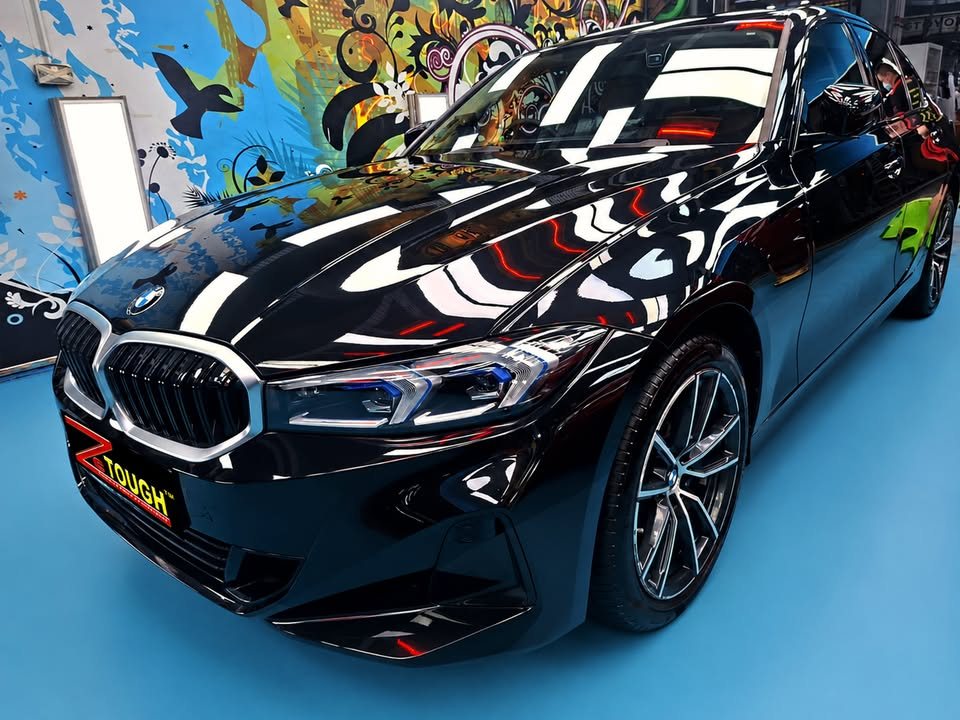 Black BMW 3 Series from the front three-quarter, workshop lights reflected across the coated bonnet.