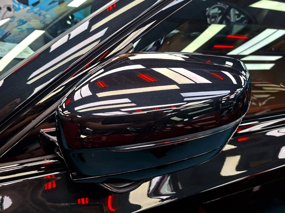 Black side mirror cap reflecting red and white workshop lights.