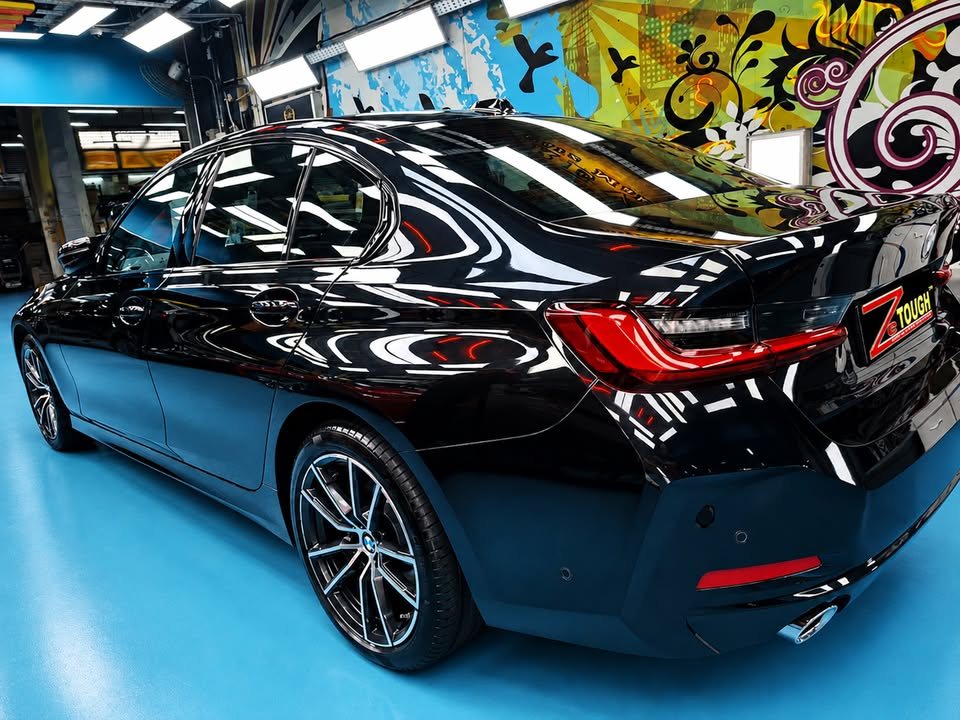 Rear three-quarter view of the black 3 Series on the blue workshop floor.