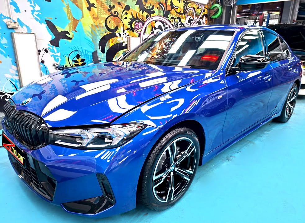 Front three-quarter view of the blue BMW 3 Series in the workshop, with black kidney grille and two-tone wheels.