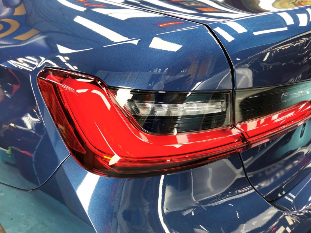 The coated bonnet of the BMW 318i under workshop lighting.