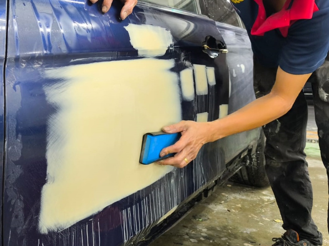 Wet-sanding the body of the BMW 318i to smooth the surface.