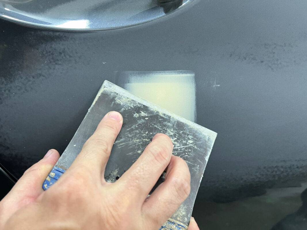 Body filler applied and worked on the BMW 320i, patching surface imperfections.