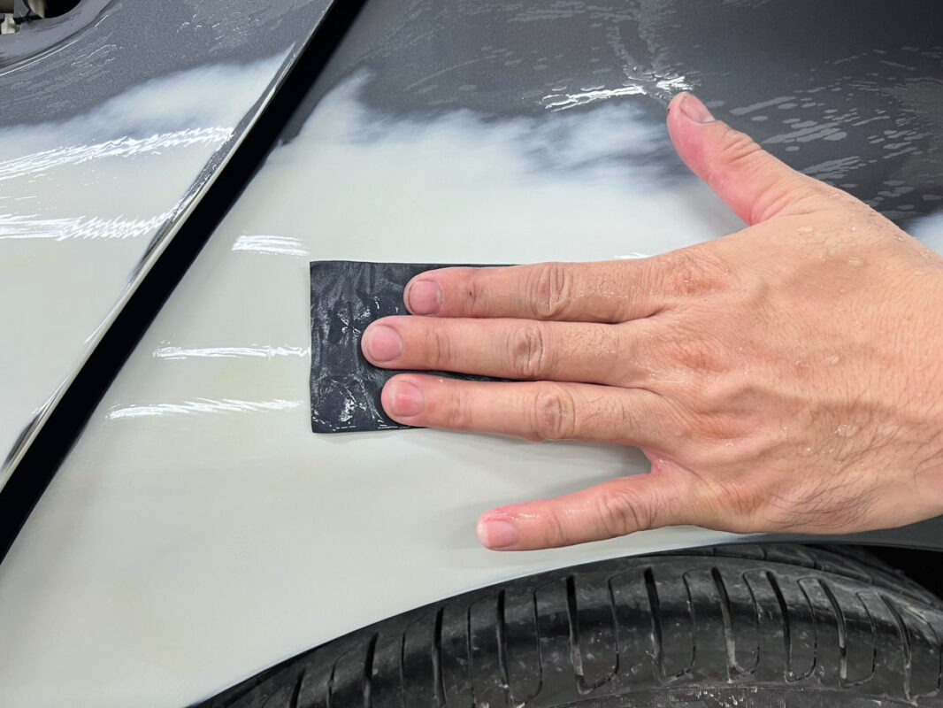 Wet-sanding the BMW 320i's bodywork to achieve a smooth, level surface.