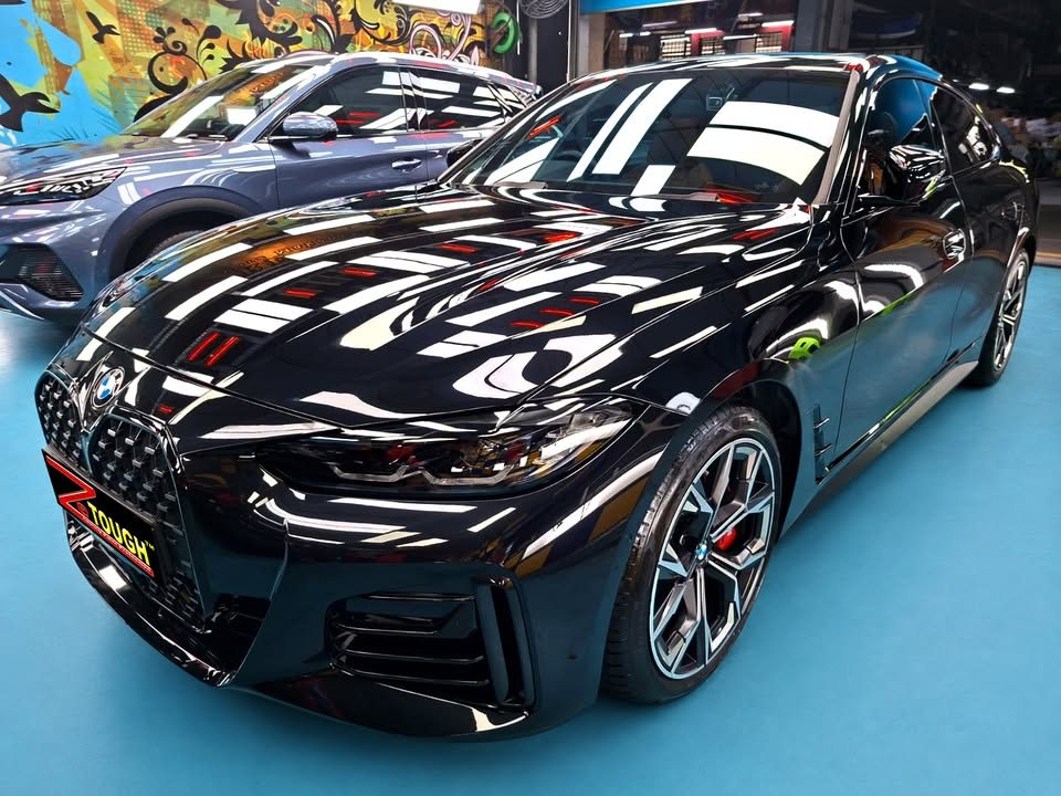 Front three-quarter view of a black BMW 4 Series Gran Coupe in the Revol Carz Makeover studio, studio lights reflected across the bonnet.