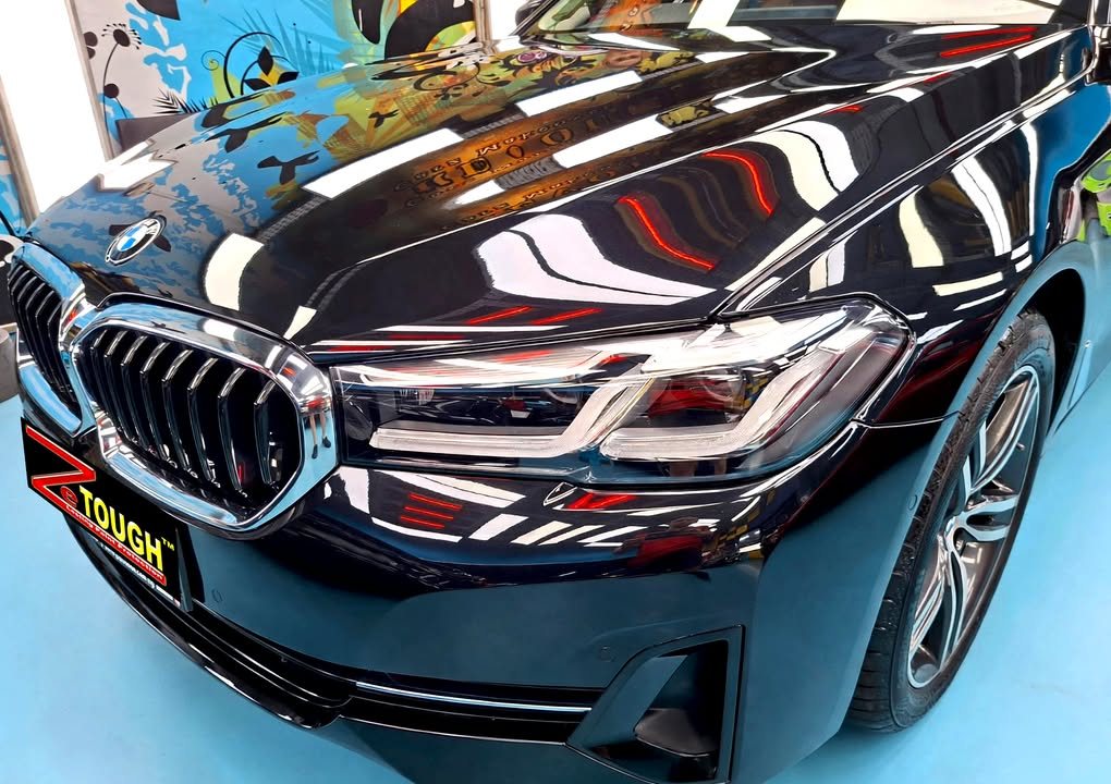 Kidney grille and headlamp of the black 5 Series with the workshop mural reflected in the bonnet.