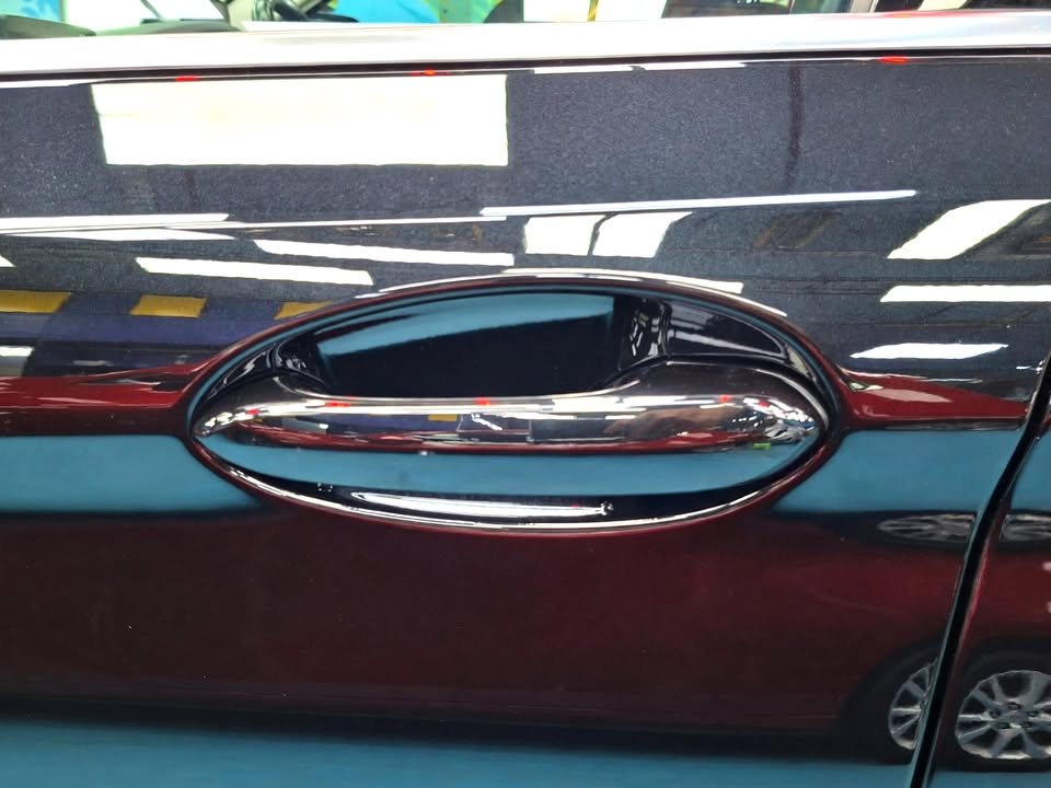 Chrome door handle on the black door panel with reflections.