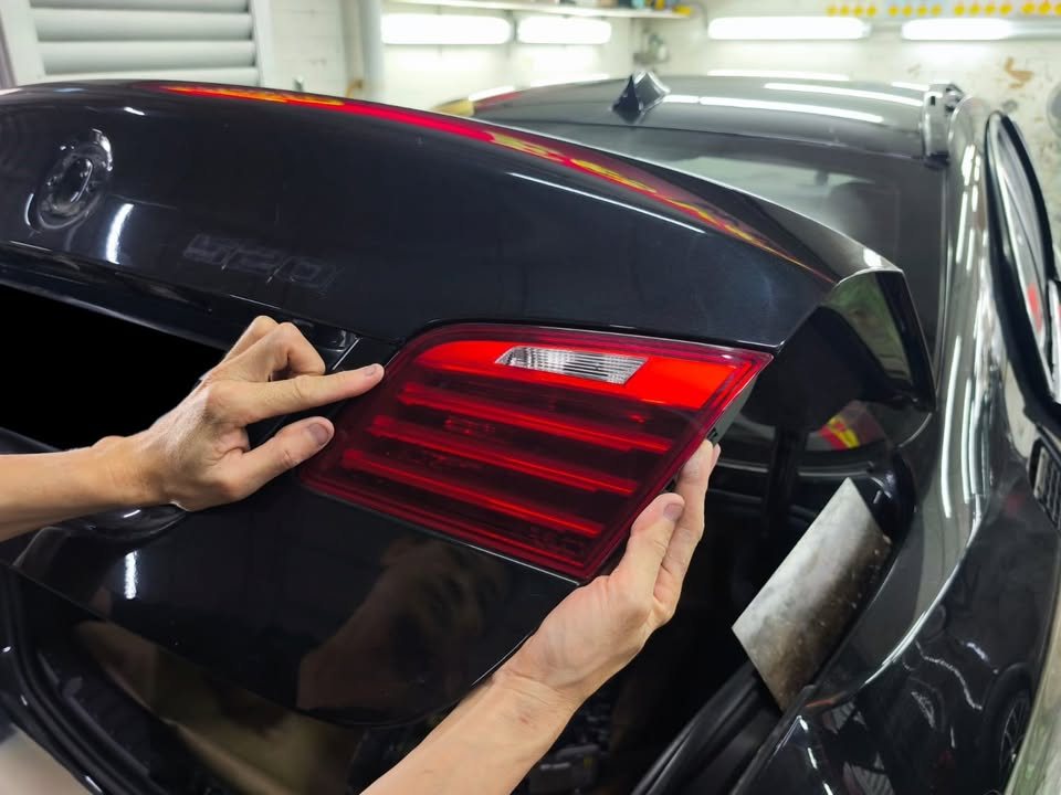Technician removing the red tail lamp from the rear of the black BMW.