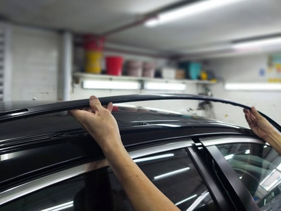 Two hands lifting the roof trim strip off the black BMW.