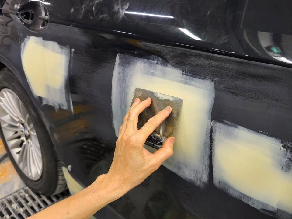 Several patches of cream filler on the BMW's side being sanded by hand.