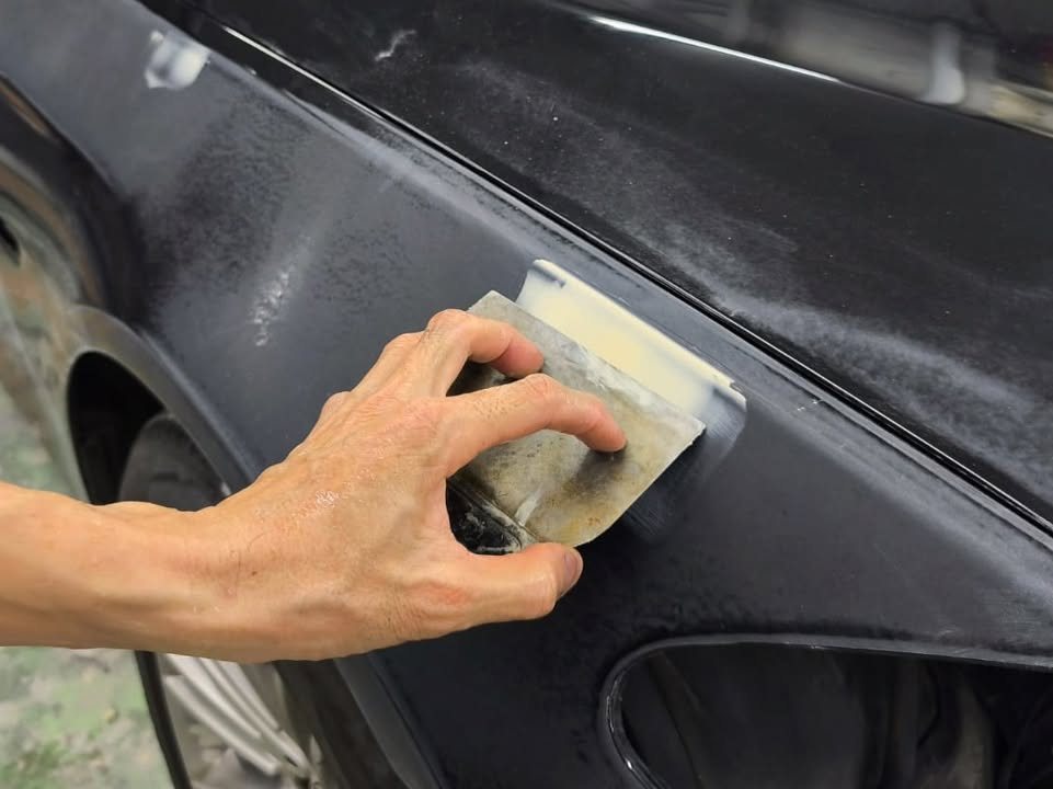 Hand sanding a filler patch on the rear wheel arch of the BMW.