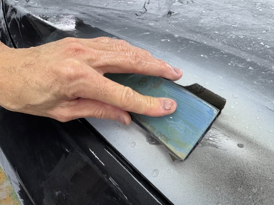 Wet sanding block moving across the grey primed surface of the BMW.