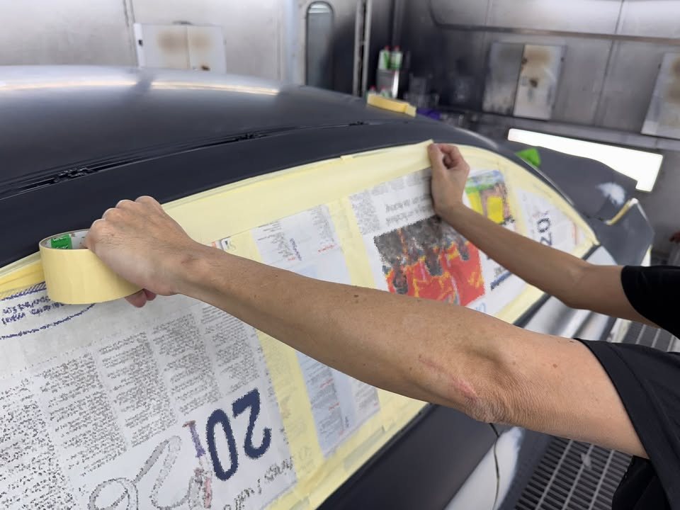 Technician masking the BMW's rear window with tape and newspaper.