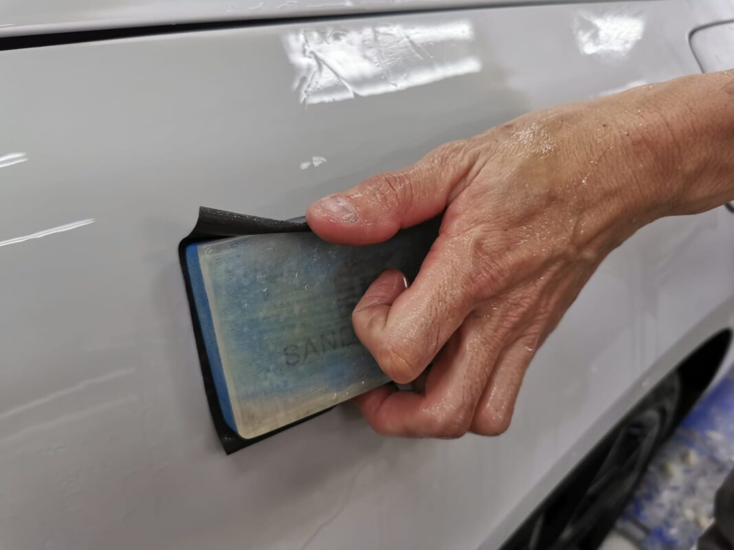 Wet-sanding continues, levelling the surface across a panel on the BMW 840i Cabriolet.