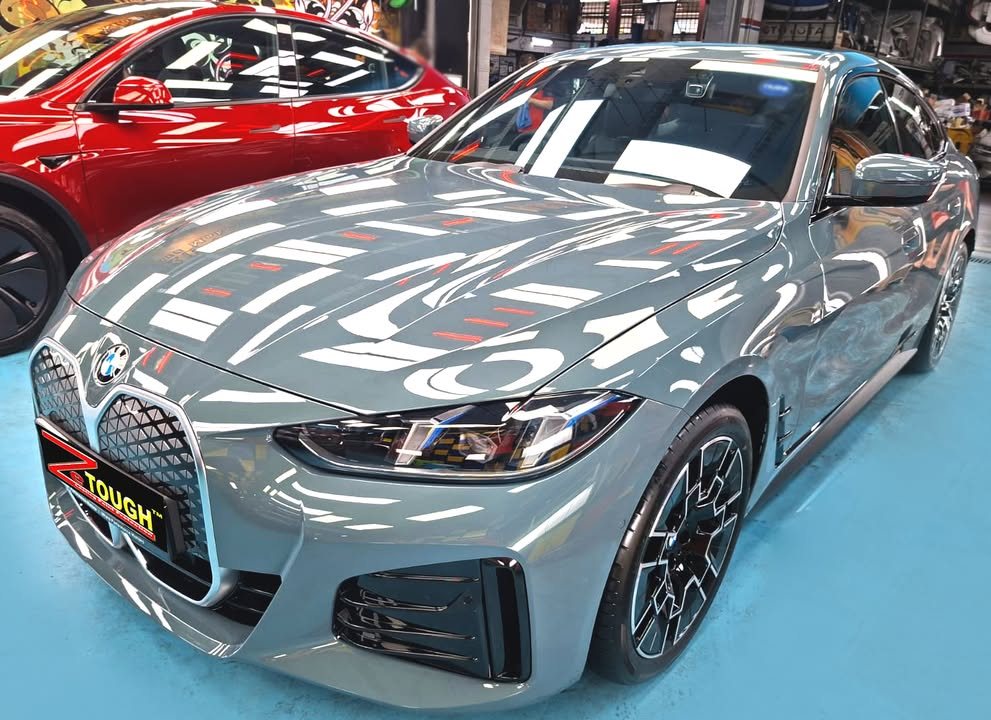 Grey BMW i4, front three-quarter view, in the Revol Carz workshop after coating, with lights reflected across the bonnet.