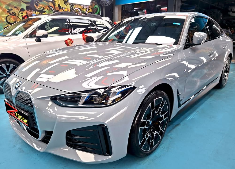 Front three-quarter view of a light grey BMW i4 Gran Coupe in the Revol Carz Makeover studio, ZeTough plate on the front bumper.