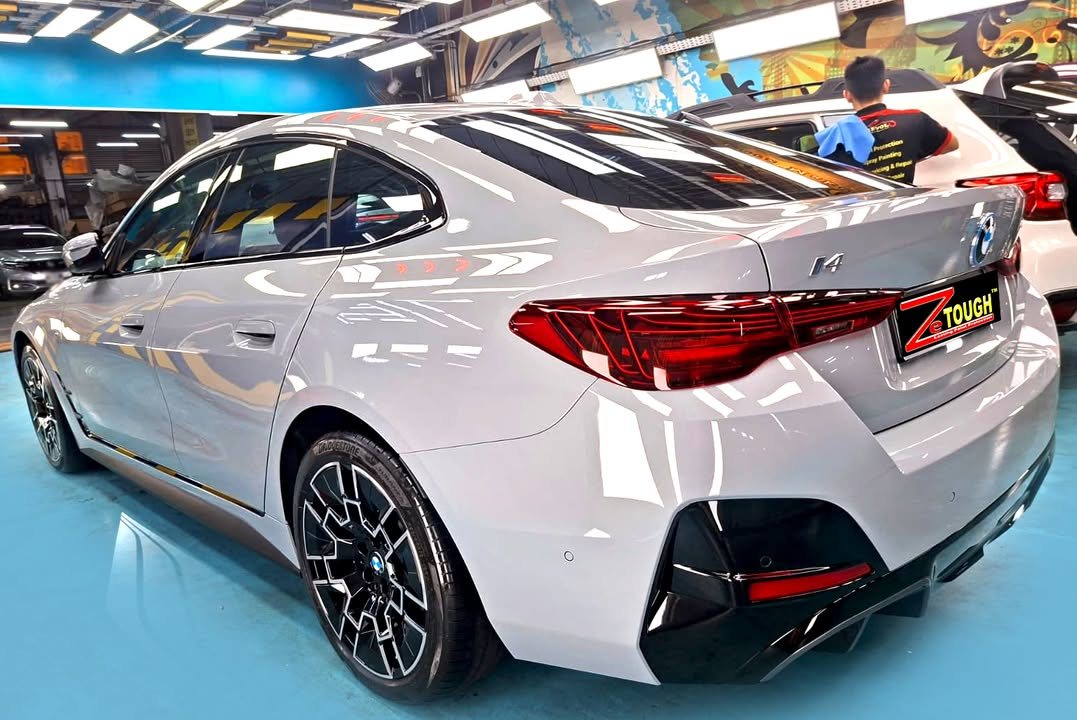 Rear three-quarter view of the light grey BMW i4 showing the tail lights and black rear diffuser.