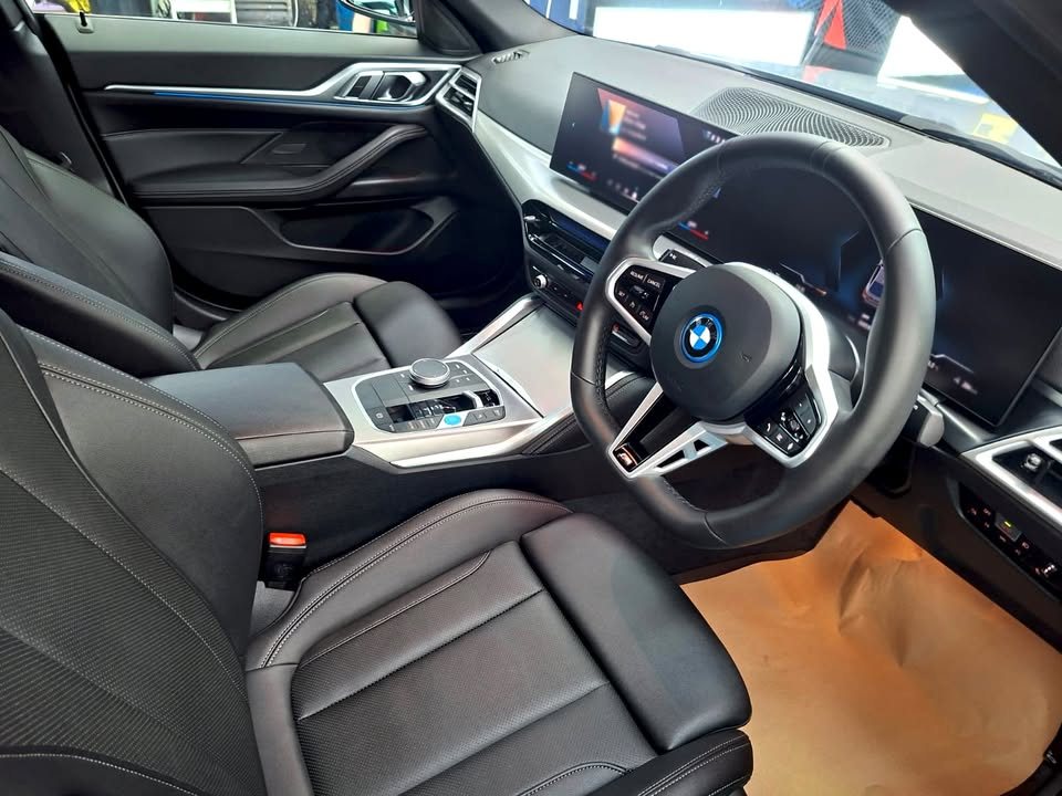 Interior of the BMW i4 with black leather seats, steering wheel and curved display.