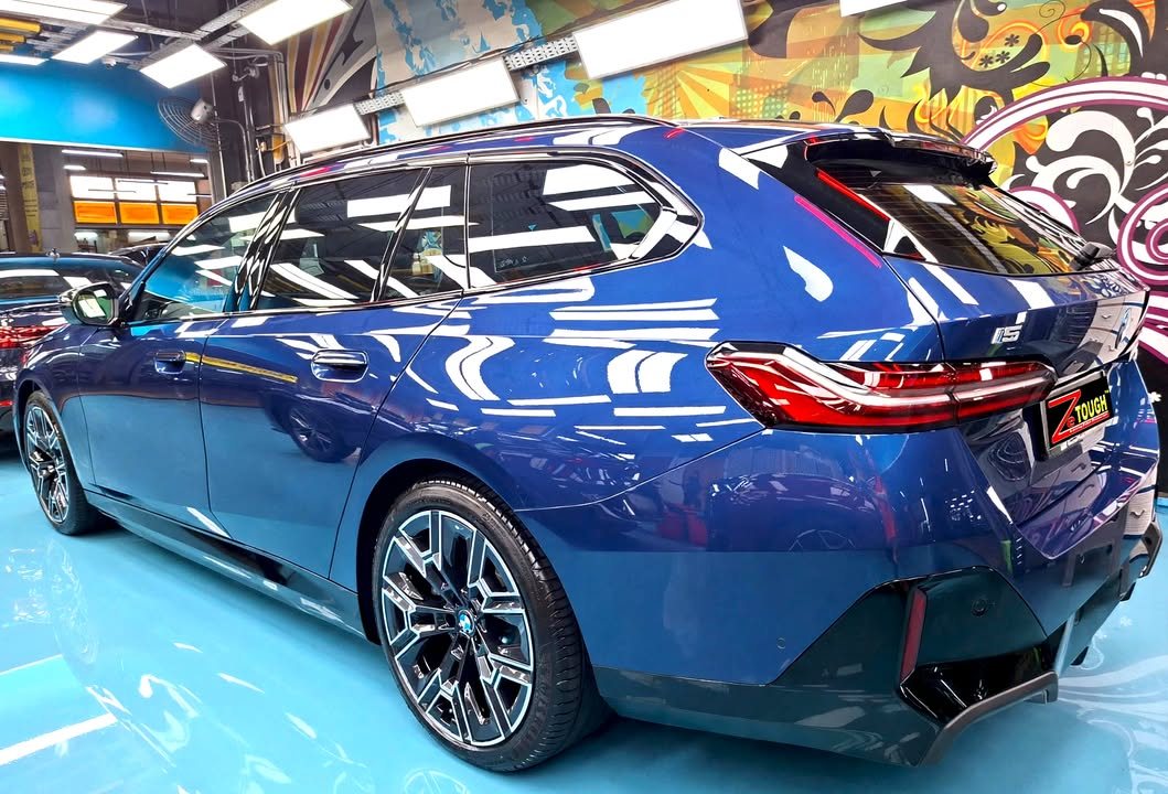 Rear three-quarter view of the blue BMW i5 estate showing the tail lights and rear diffuser.