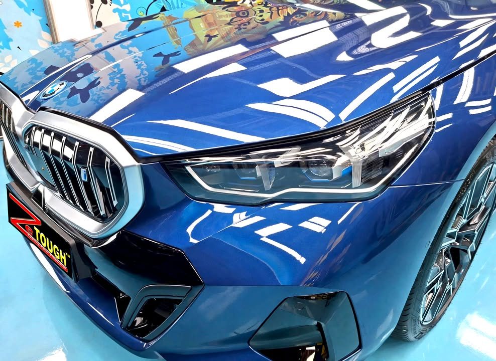 Close-up of the BMW i5 kidney grille and headlight, with studio lights reflected in the blue bonnet.