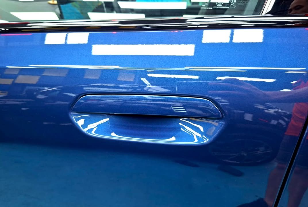 Close-up of the blue door panel and handle reflecting the workshop lights.