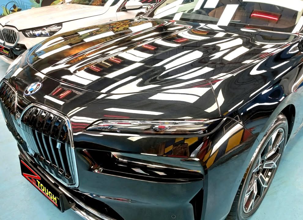 Front of the black i7 with ceiling lights reflected across the bonnet and grille.