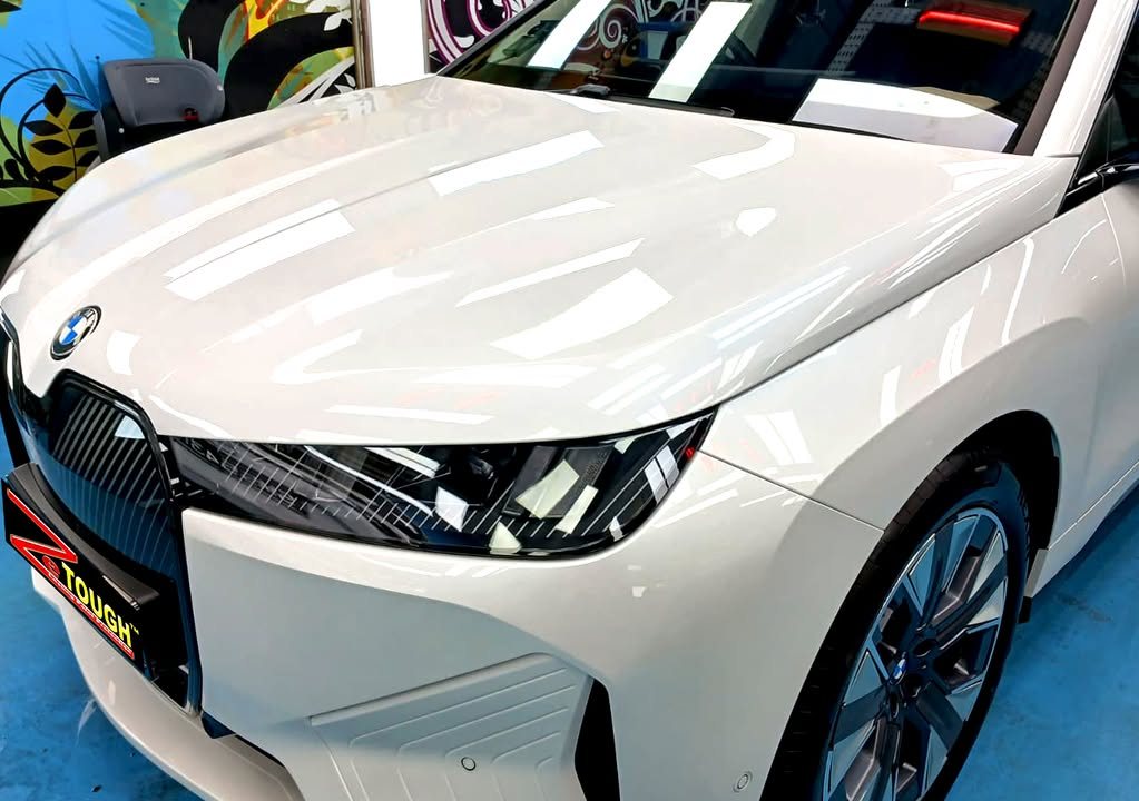 White bonnet and kidney grille of the BMW iX reflecting the ceiling lights.