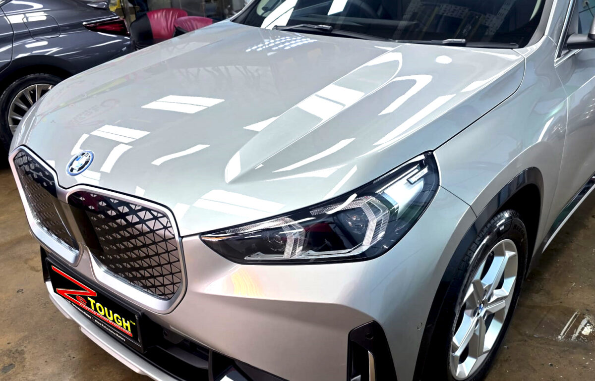 The BMW iX1's coated paintwork under workshop lighting.