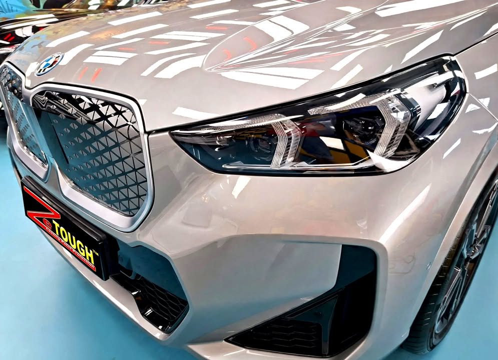 Close-up of the BMW iX1 kidney grille and headlight, with studio lights reflected in the silver bonnet.