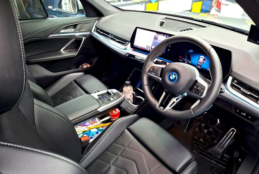 Interior of the BMW iX1 showing the black leather seats, steering wheel and curved display.