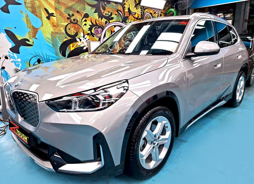 Front three-quarter view of a silver BMW iX1 in the Revol Carz Makeover studio, ZeTough plate on the front bumper.