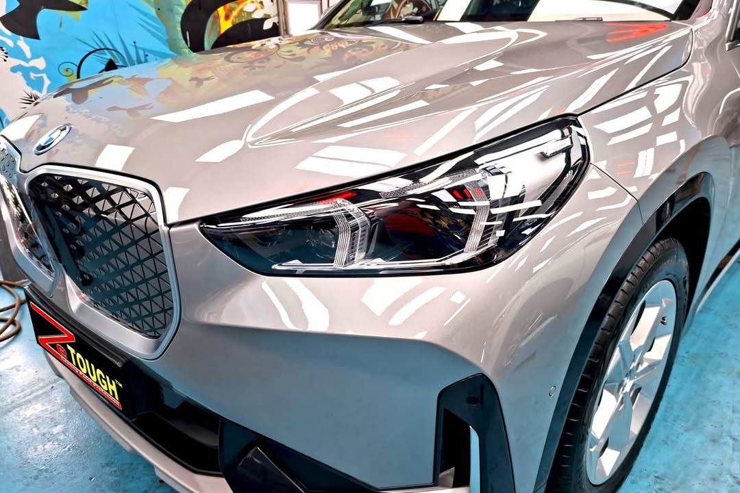 Close-up of the BMW iX1 kidney grille and headlight with lights reflected in the silver bonnet.