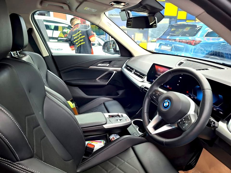Interior of the BMW iX1 with black leather seats, steering wheel and curved display.