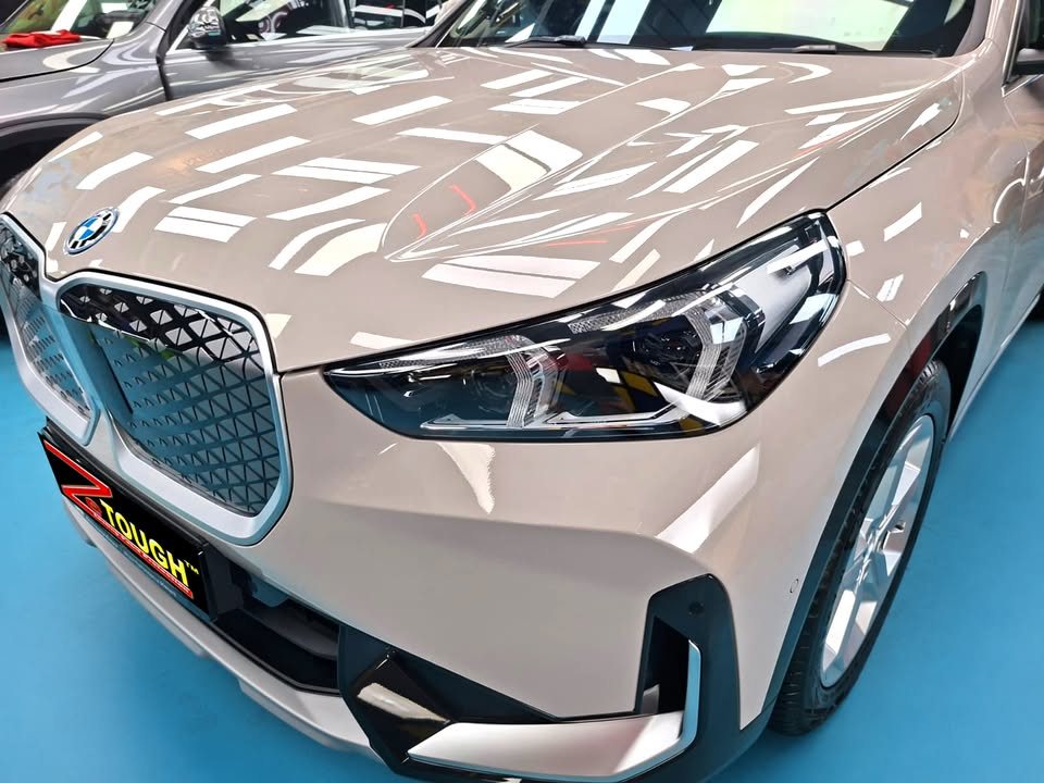 Front of the beige BMW iX1 showing the kidney grille, headlamp and bonnet reflections.