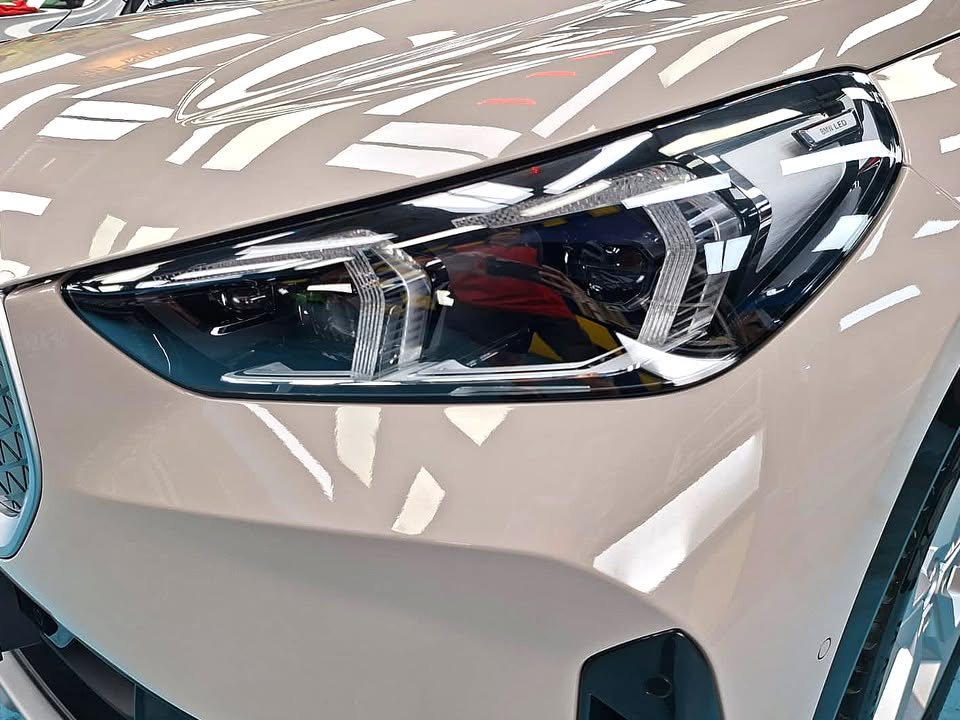 Close-up of the BMW iX1 headlamp and beige front wing.